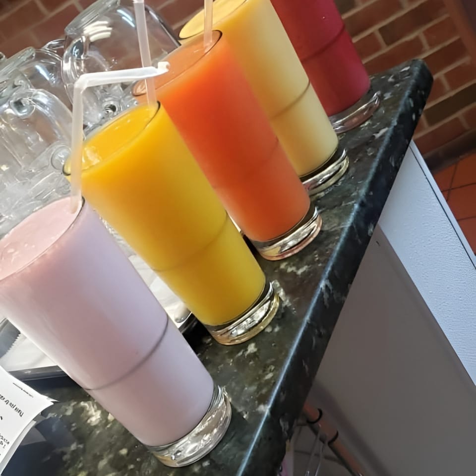 Five colorful Ecuadorian fruit juices and milkshakes in tall glasses with straws on a counter.