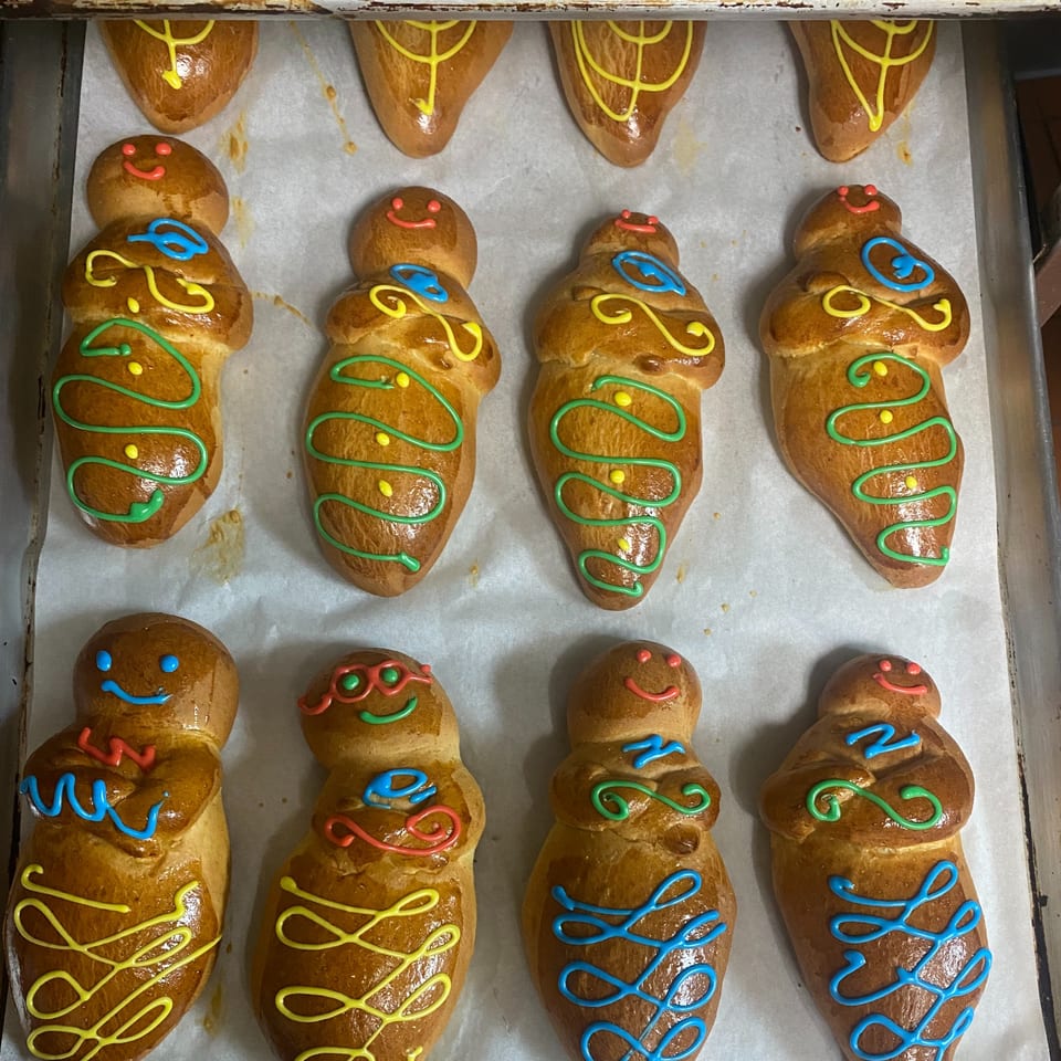 Rows of Ecuadorian guaguas de pan, sweet bread dolls decorated with colorful icing, on a baking sheet.