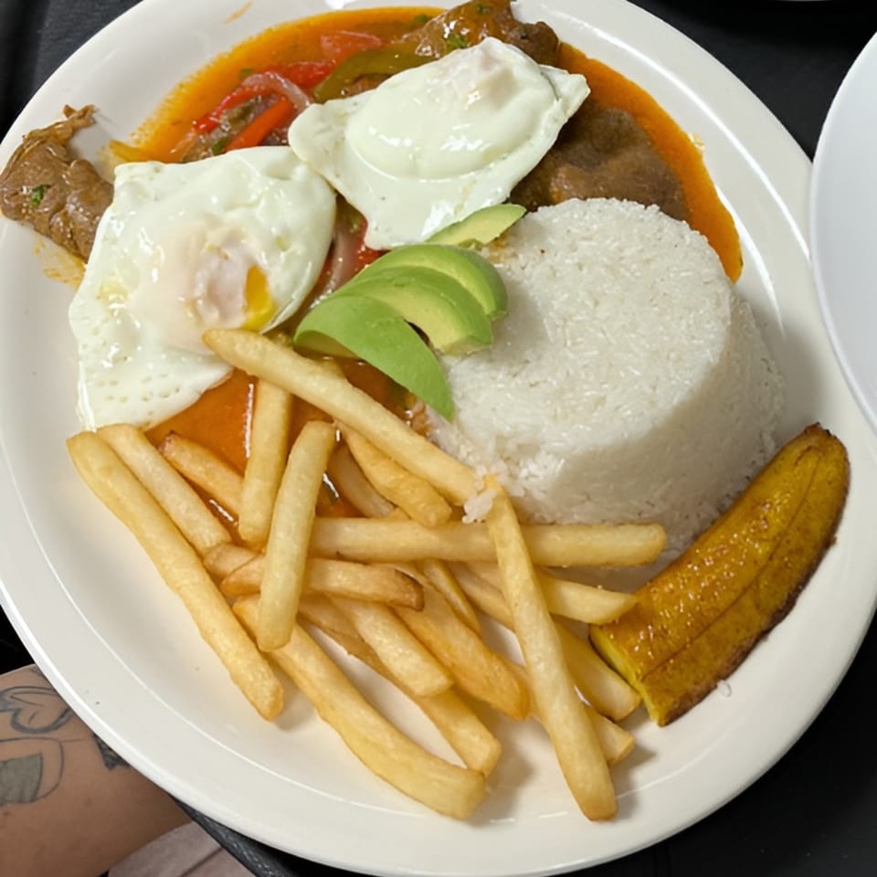 Ecuadorian dish with steak, fried eggs, rice, avocado, french fries, and a plantain on a white plate.