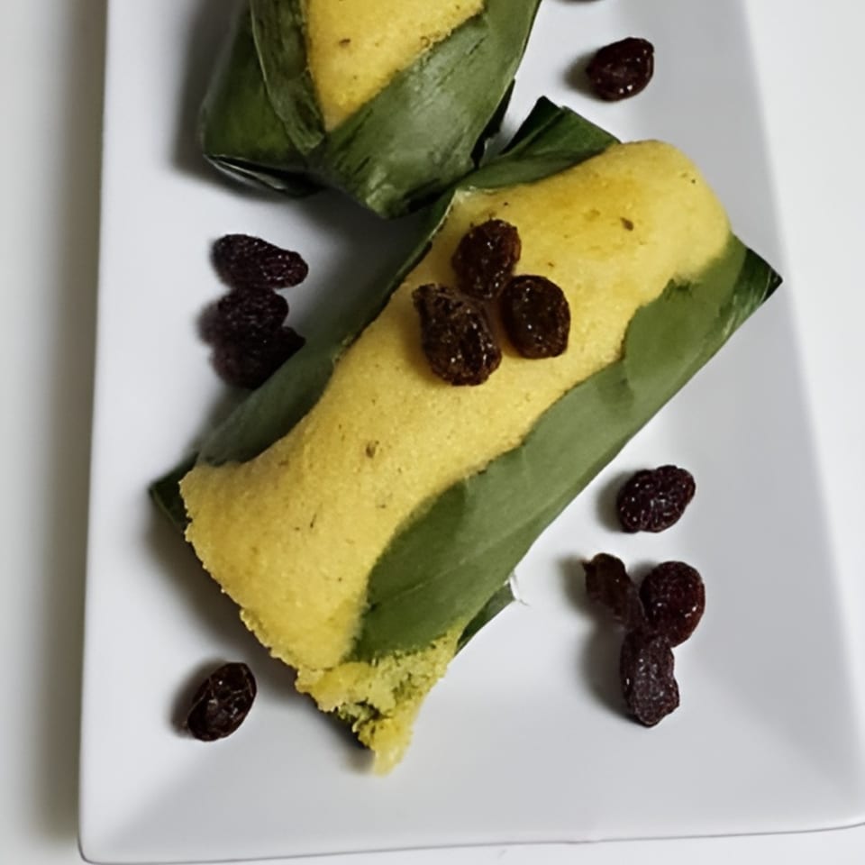 Two Ecuadorian humitas, a savory corn cake wrapped in a corn husk, garnished with raisins on a white plate.